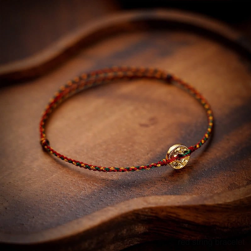 Natural red string anklet with braided weave and gold coin displayed on curved wooden tray