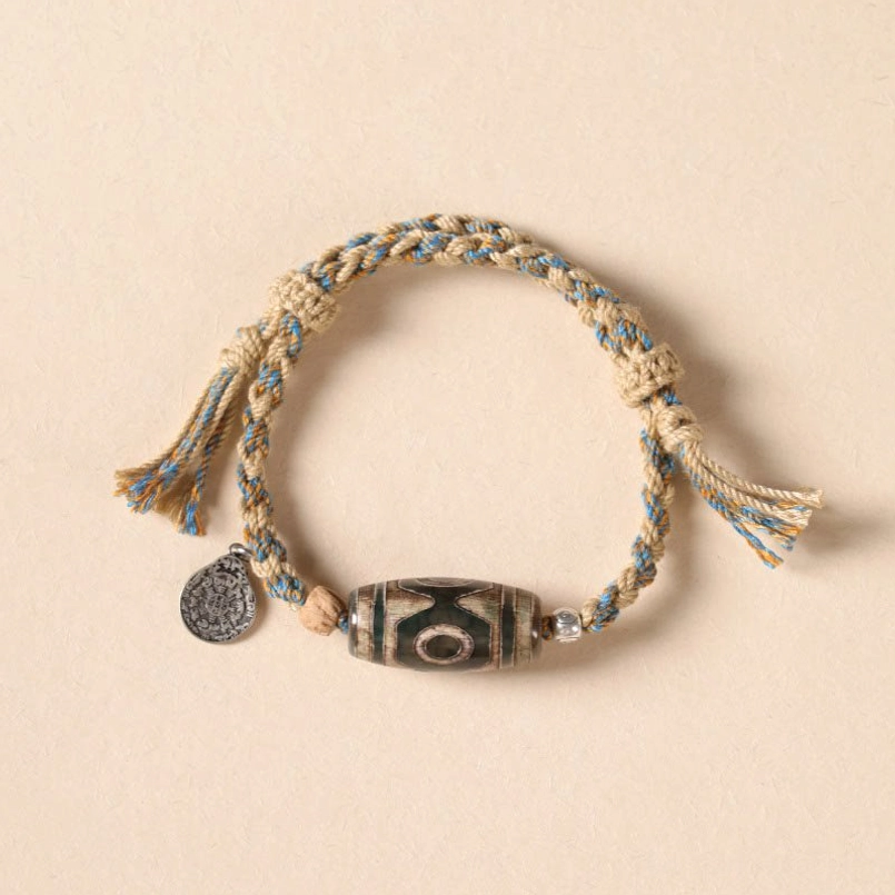 Nine-Eye Dzi Bead wealth protection braided bracelet top view on beige background