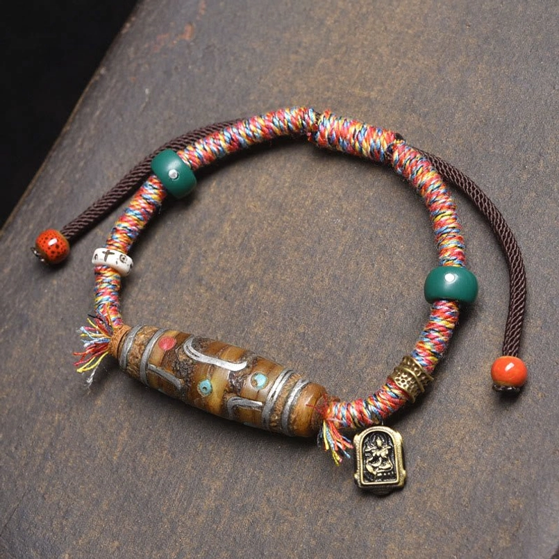 Nine-eye Dzi bead protection bracelet overhead flat lay with mixed braided cords and metal Buddha charm