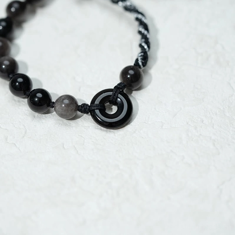 Overhead close-up of black obsidian peace buckle bracelet showing clarity of peace buckle charm and woven rope design