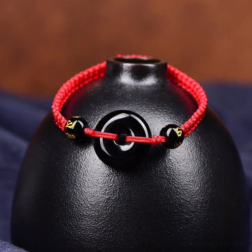 Red Obsidian Peace Buckle bracelet front view with engraved beads on ceramic display