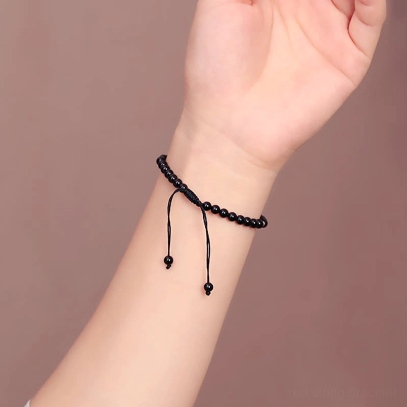 Slim black obsidian beaded bracelet on wrist against warm tone background with long adjustable tassel