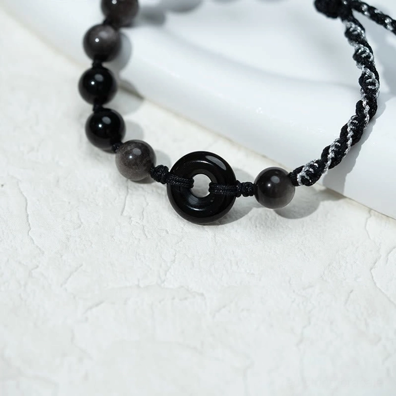 Detailed side view of black obsidian peace buckle bracelet showcasing bead texture and braided rope craftsmanship on smooth white surface