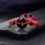 Black Obsidian Peace Buckle bracelet with red braided cord close-up on stone tray