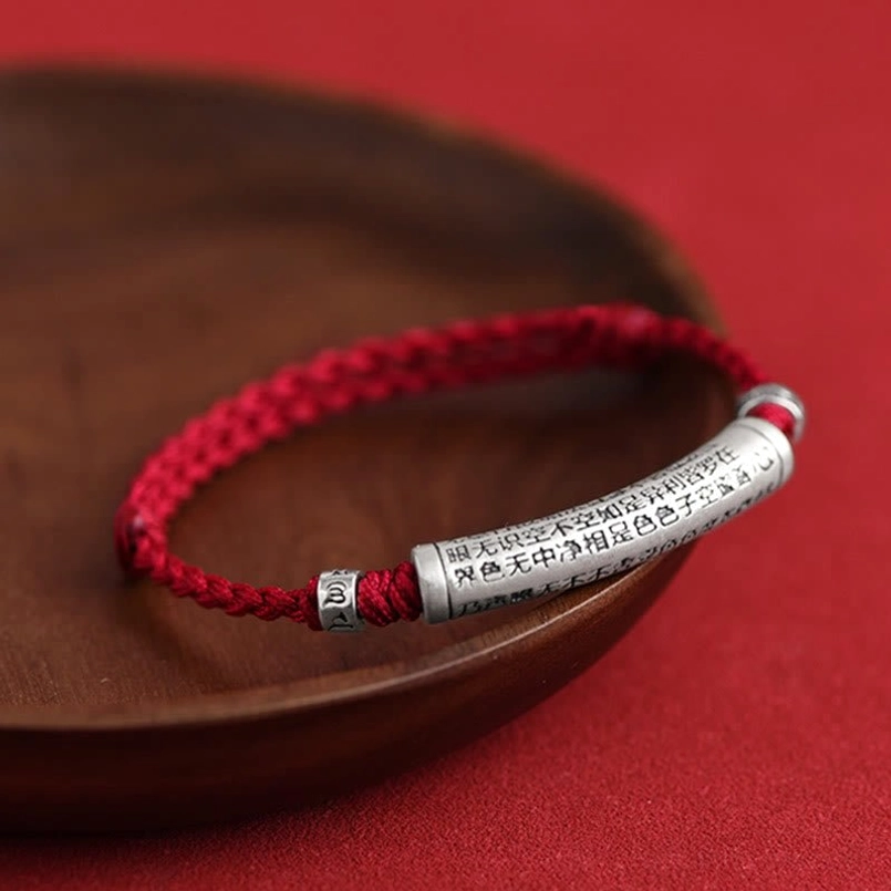 Woven red rope bracelet with 3D carved silver pendant side close-up on wooden tray
