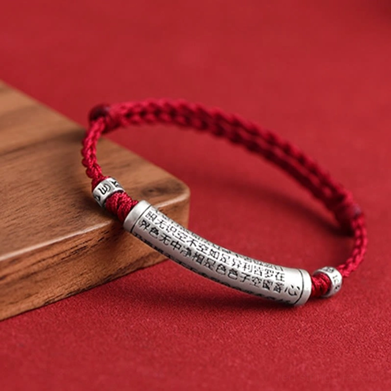 Red string Buddhist bracelet with 999 silver pendant displayed on wooden block prop