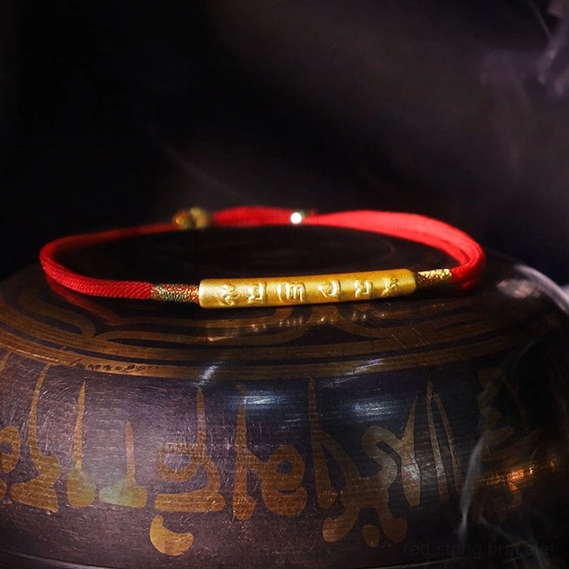 Tibetan red string bracelet with gold engraved Om Mani Padme Hum bead displayed on singing bowl background