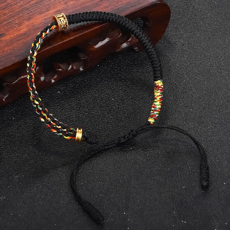 Om Mani Padme Hum black protection bracelet with gold mantra charm - side angle on wooden display