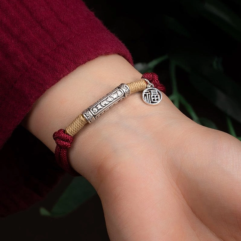 red and beige braided lucky bracelet worn on wrist with silver engraved charm close-up