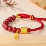 Om Mani Padme Hum cinnabar red string bracelet with sterling silver charm, flat lay on tan desktop with dried flowers