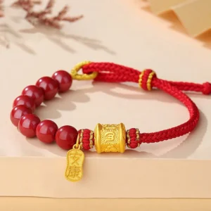 Om Mani Padme Hum cinnabar red string bracelet with sterling silver charm, flat lay on tan desktop with dried flowers