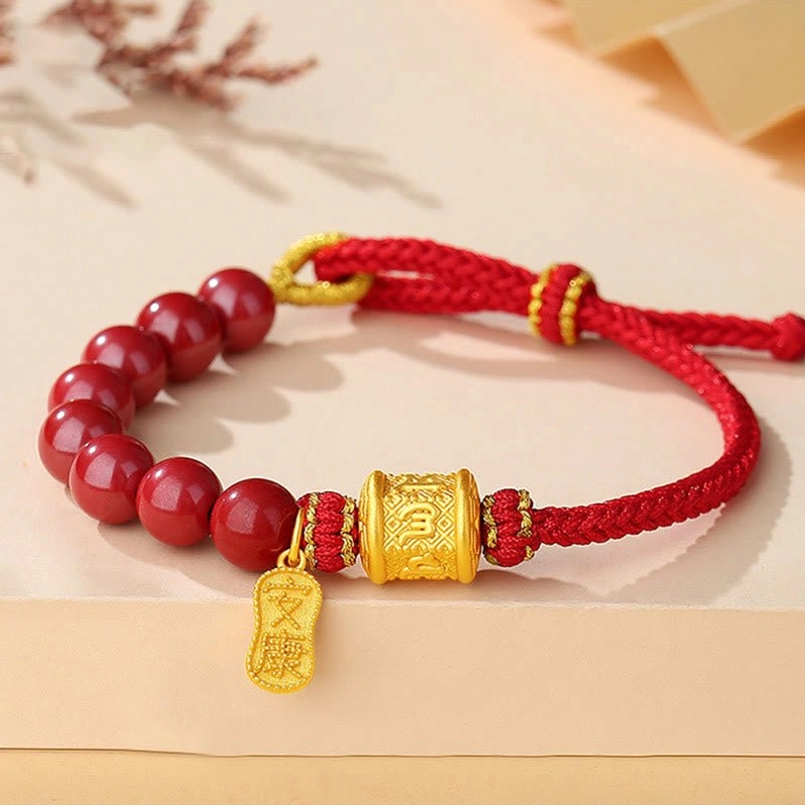 Om Mani Padme Hum cinnabar red string bracelet with sterling silver charm, flat lay on tan desktop with dried flowers