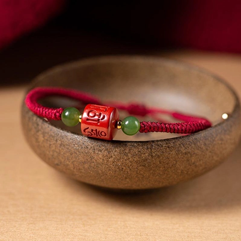 Red braided Tibetan bracelet resting in ceramic bowl, cinnabar and jade beads visible