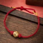 Hand-woven Om Mani Padme Hum red string bracelet with gold mantra bead on dark wooden surface