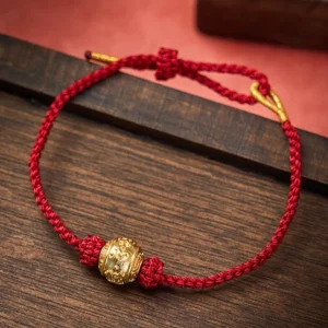 Hand-woven Om Mani Padme Hum red string bracelet with gold mantra bead on dark wooden surface