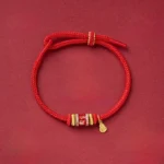 Om Mani Padme Hum red string bracelet with copper beads, top-down flat lay view on dark background