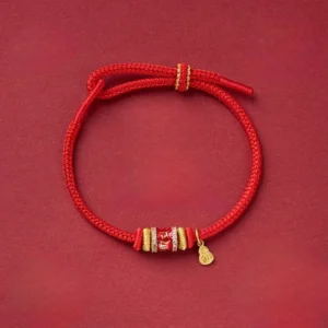Om Mani Padme Hum red string bracelet with copper beads, top-down flat lay view on dark background