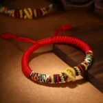 Om Mani Padme Hum red string bracelet with golden King Kong knot on wooden desk background
