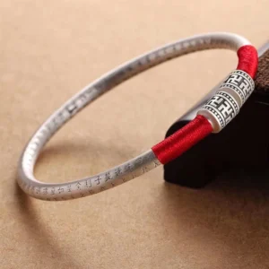 Om Mani Padme Hum red string bracelet with engraved silver charm on wooden surface - top view