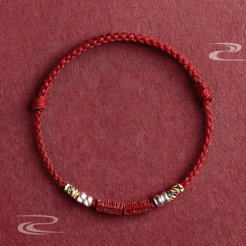 Om Mani Padme Hum red string bracelet with carved cinnabar bead and sterling silver accents, flat lay top view