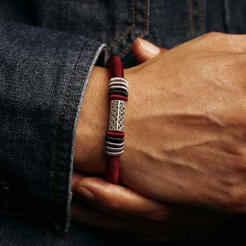 Red Om Mani Padme Hum bracelet worn on wrist, close-up view showing intricate silver charm engraving