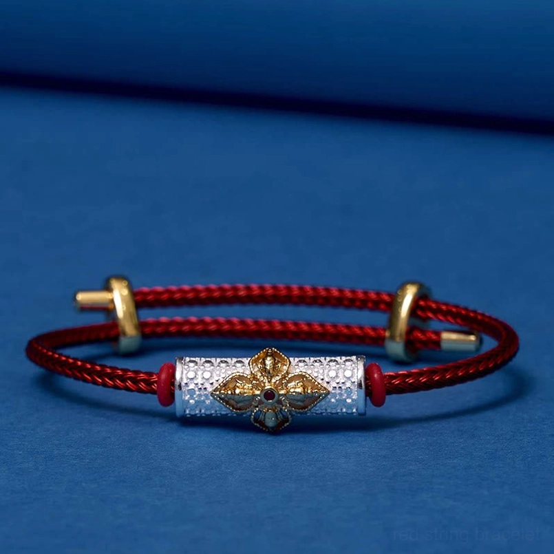 Luck bracelet with red cord and ornate copper flower bead on display surface