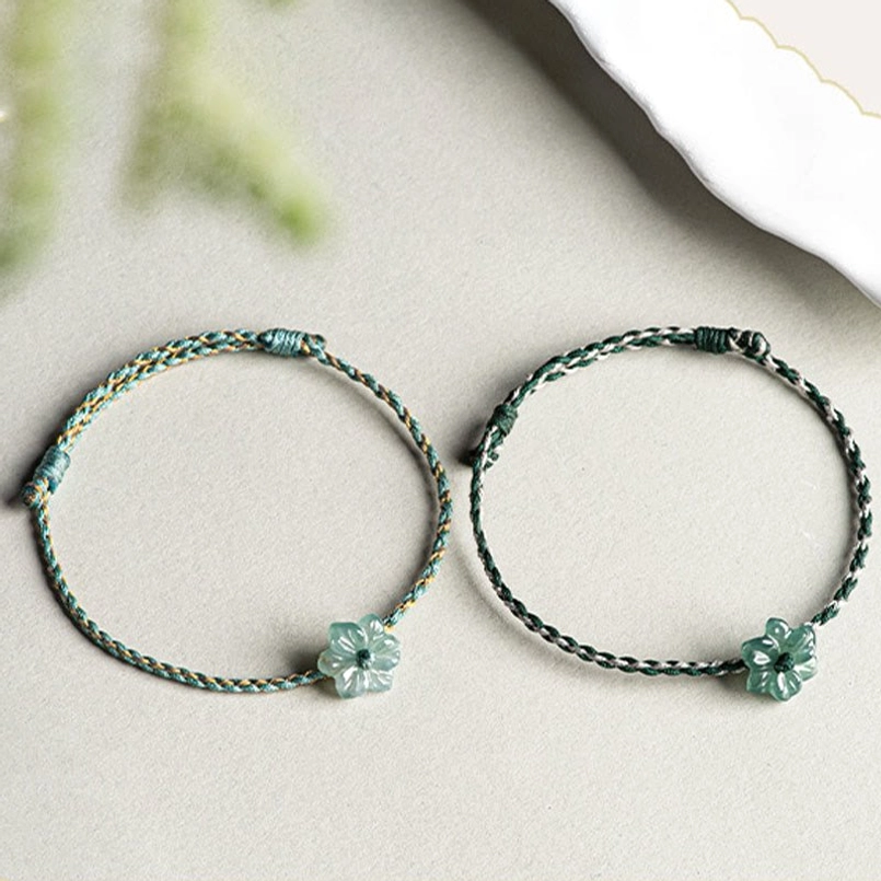 Pair of dark green string jade orchid prosperity bracelets on light fabric backdrop