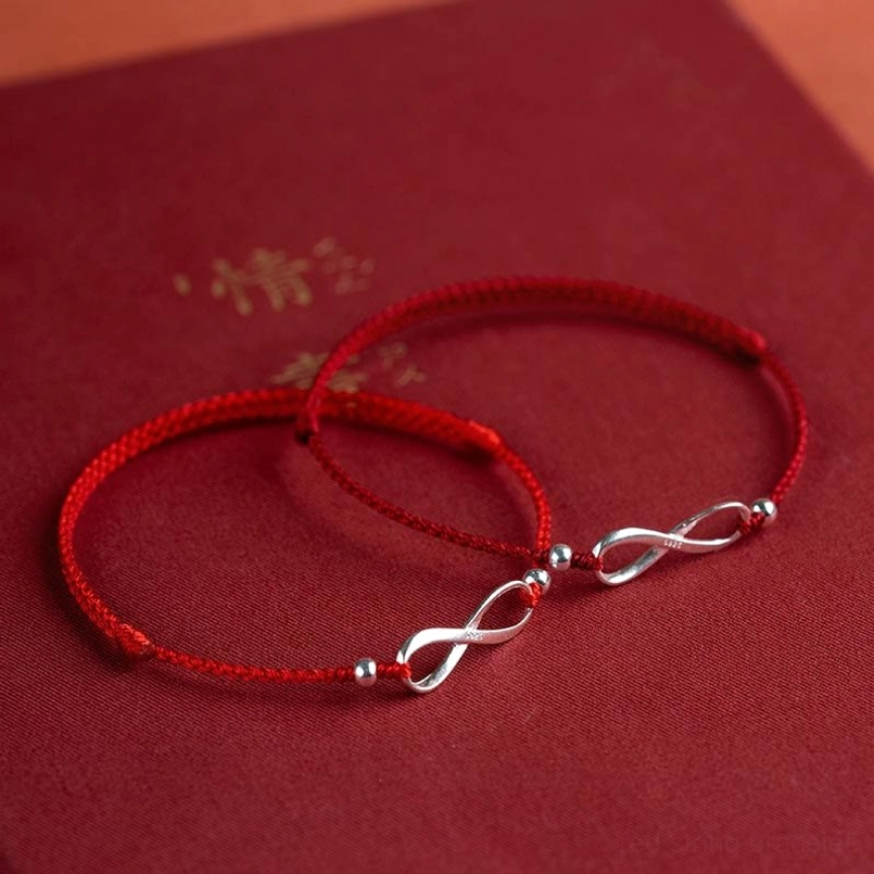 Twin red string bracelets with endless knot silver charms on golden book