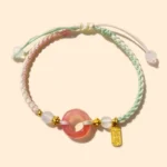 Peace buckle agate red string bracelet with gold charm, dual-tone woven cord, top-down view