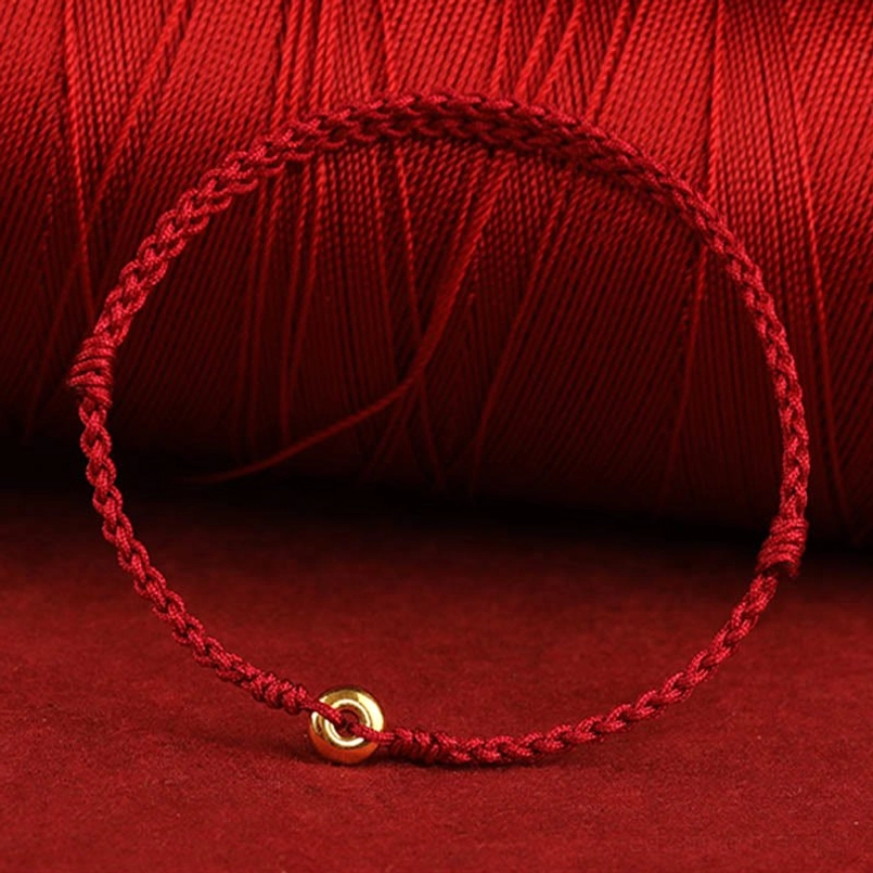 braided red cord fortune bracelet with central gold charm on thread background