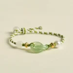 Green and white braided peace buckle bracelet overhead view with jade charm and gold accents