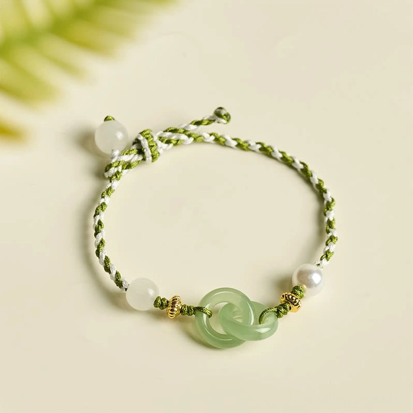 Peace buckle jade bracelet with braided rope and pearl accents flat lay on natural leaf background