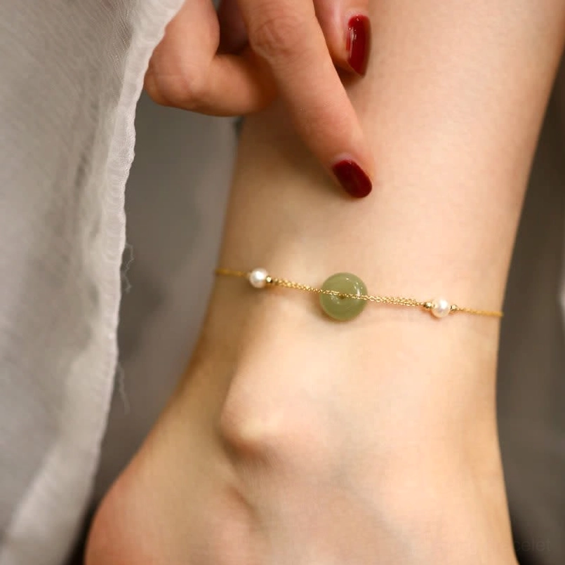 Close-up detail of peace buckle jade charm with pearl accents on adjustable cord anklet