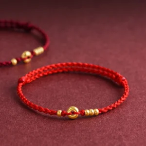 Red braided peace buckle luck bracelet with gold beads and handwoven rope on burgundy fabric