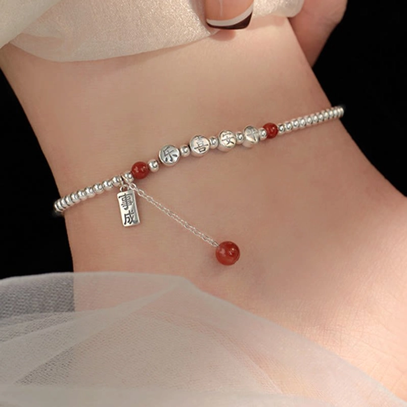 Peace and joy blessing anklet with dangling red tassel charm worn on ankle with fabric backdrop