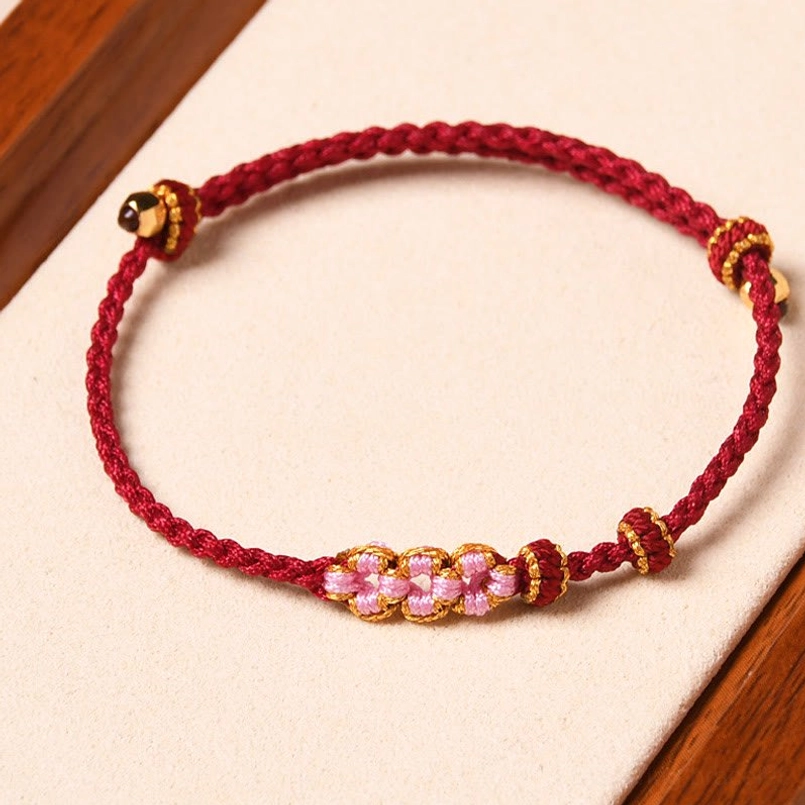 Red woven peach blossom protection bracelet flat lay with floral beads and gold hardware