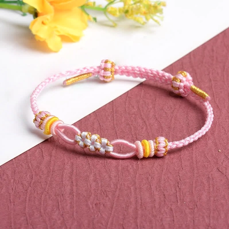 Pink handmade peach blossom bracelet with white and gold decorative knots adjustable cord flat lay