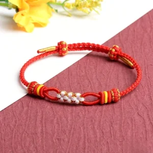 Red handmade peach blossom knot luck bracelet with white and gold accents on red-white background with yellow flowers