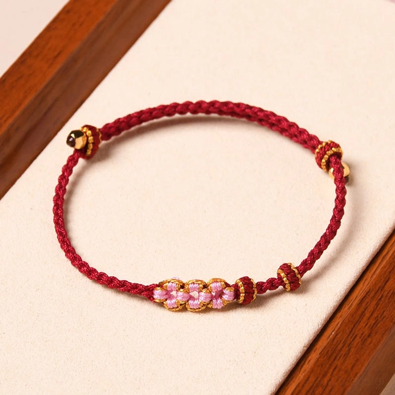 Red braided flower protection bracelet with pink peach blossom charms and gold accents