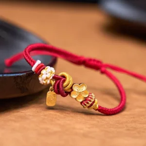 Peach blossom red string bracelet with gold flower charm and fu pendant on wooden table