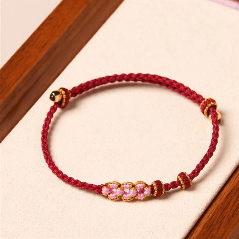 Handmade peach blossom red string protection bracelet with gold flower charms overhead view