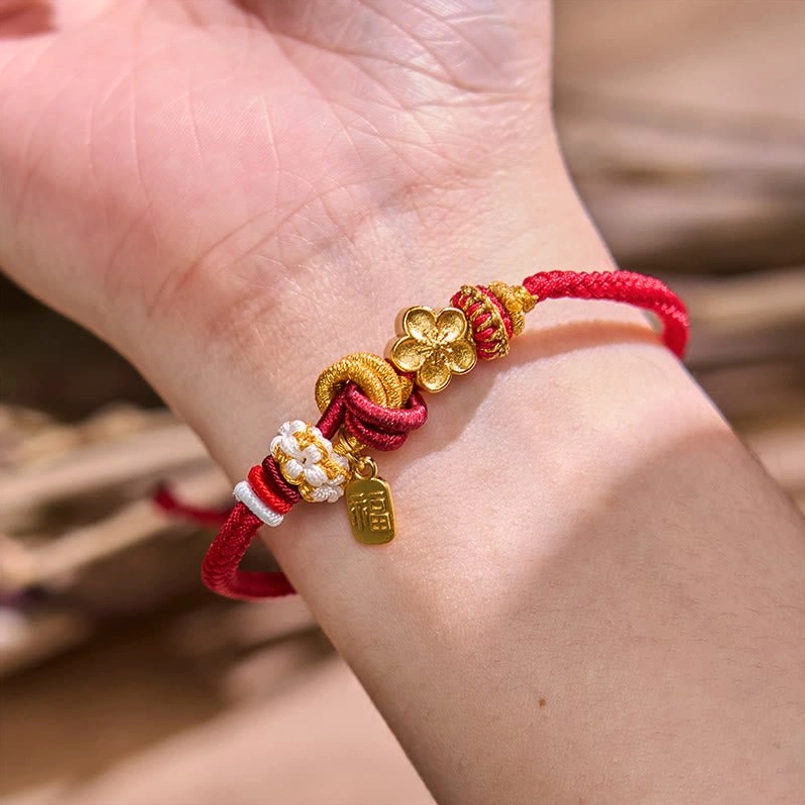 Red string bracelet worn on wrist showing peach blossom charm and decorative knots