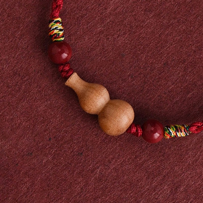 Close-up detail of peach wood gourd charm with red beads and braided rope accents
