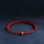 Natural peach wood bead red string bracelet with twisted braided cord on dark blue background