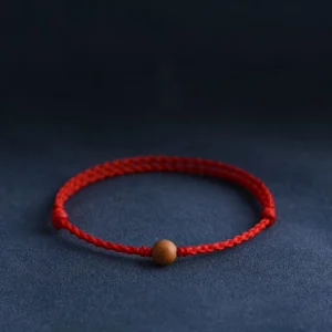 Natural peach wood bead red string bracelet with twisted braided cord on dark blue background