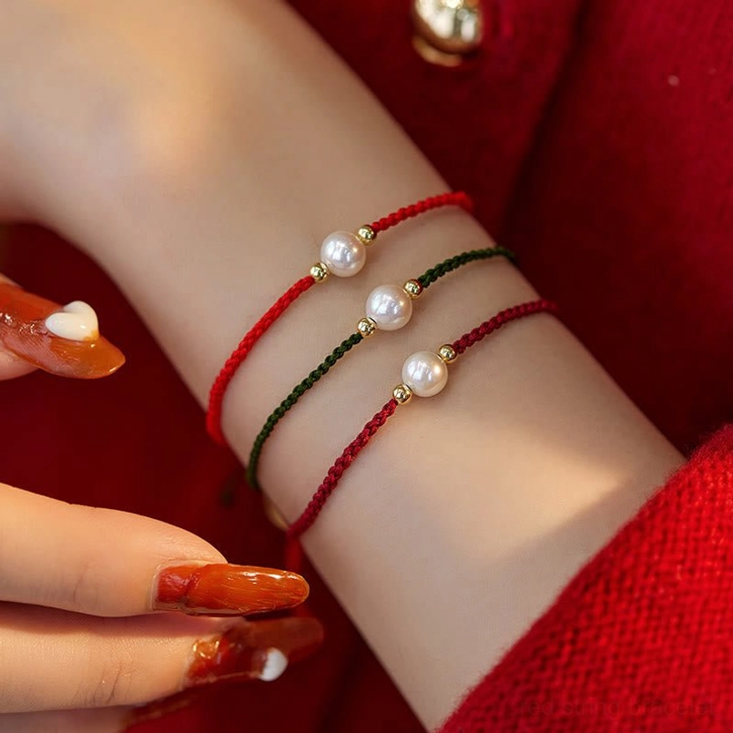 Pearl red string bracelet worn on wrist close-up side view with red knitwear background