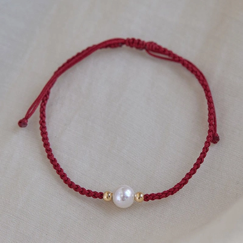 Pearl string bracelet flat lay burgundy red cord central white pearl gold beads pull closure