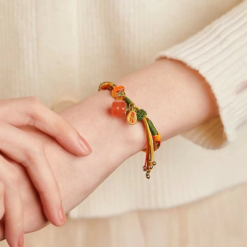 Persimmon agate reincarnation bracelet worn on wrist with decorative tassel against soft background