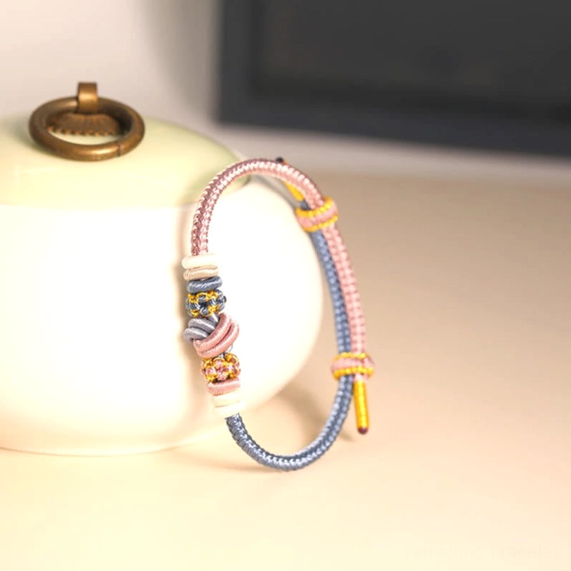 Pink and blue handcrafted peace knot bracelet with Chinese disk knot details displayed with ceramic prop