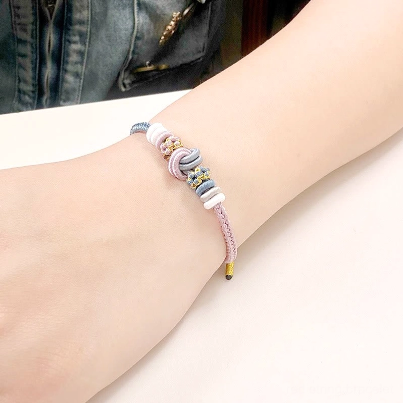 Eight thread peace knot bracelet in light pink and blue worn on wrist with denim clothing background casual daily wear